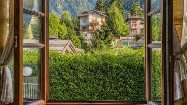 A window with a view of a mountain landscape, a building with balconies, and a hedge in the foreground. - Le Ville Apartment - Ponte di Legno (Ponte di Legno)