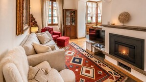 A living room with a fireplace, a sofa, a television, and a patterned rug. - Le Ville Apartment - Ponte di Legno (Ponte di Legno)
