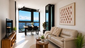 A modern living room with a sofa, coffee table, TV, and a dining area with chairs and a table. - 63 Floors Up & A Million-Dollar View 2BR w/ Carpark (Brisbane City)