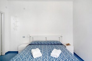 Une chambre à coucher avec un lit, deux tables de chevet, une lampe fixée au mur et une porte.