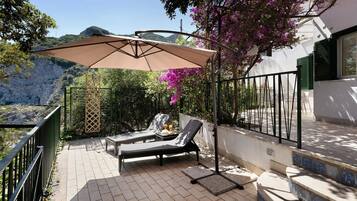 Un espace extérieur ensoleillé, aménagé avec une table, deux fauteuils et un grand parasol.