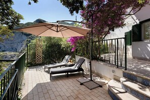 A sunlit outdoor seating area with a table, two lounge chairs, and a large umbrella.