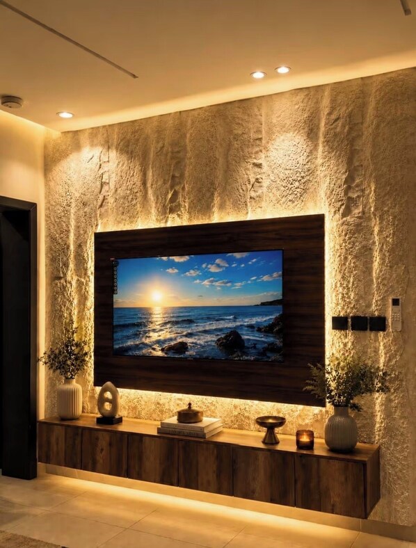A wall-mounted TV with a coastal sunset view, a wooden console below, and textured stone wall.