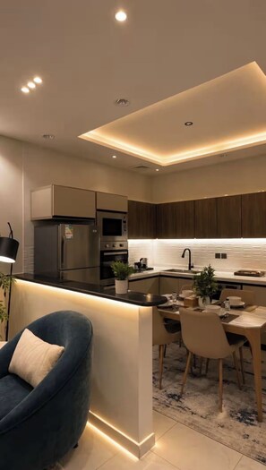 A modern kitchen with built-in appliances, a dining area with a table and chairs, and a blue armchair.