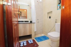 Ein Badezimmer mit Toilette, Waschbecken, Dusche und einem Paar Flip-Flops auf einer Matte.