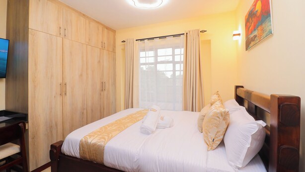 A hotel room with a bed, wooden wardrobe, a desk, and a television. - Studio in Nairobi South B (Nairobi)