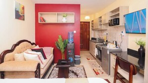 A compact living space with a sofa, a small table, a water dispenser, a television, and a kitchenette. - Studio in Nairobi South B (Nairobi)