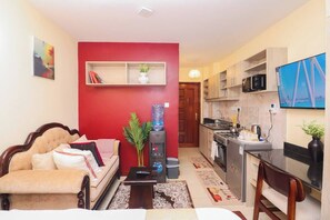 Ein kompakter Wohnraum mit Sofa, einem kleinen Tisch, Wasserspender, Fernseher und einer Küchenzeile.