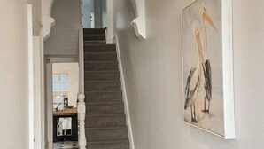 Un pasillo con una escalera, una lámpara colgante y un cuadro de pájaros en la pared.