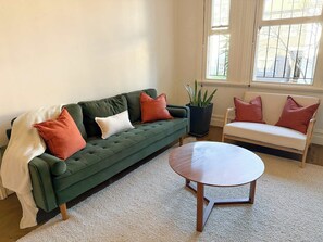 A green sofa with multiple cushions, a round wooden coffee table, and a white chair with cushions. - Huge Heritage Terrace, Walk to KX, Parking, BBQ (Darlinghurst)
