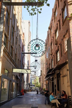 A narrow street with buildings on either side, a large clock structure hanging from the ceiling, and people sitting at outdoor tables. - Huge Heritage Terrace, Walk to KX, Parking, BBQ (Darlinghurst)