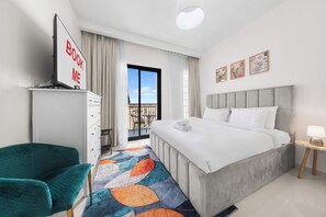 A hotel room with a bed, a desk, a chair, a balcony with a view, and artwork on the wall.
