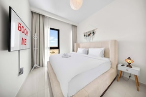 A modern hotel room with a large bed, a TV mounted on the wall, a bedside table with a lamp, and a view of the desert through the window.