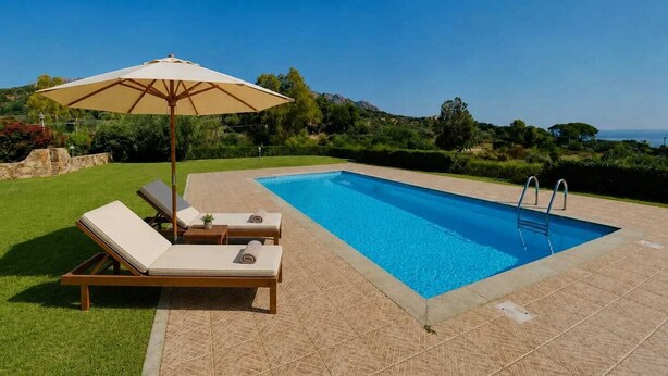 A rectangular swimming pool with a clear blue water, surrounded by a tiled deck. There are two lounge chairs and a large umbrella providing shade. - Mandy and Dolly's house with sea view and pool (tertenia)