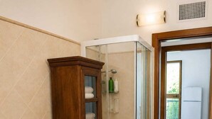 A bathroom with a wooden cabinet, a glass shower enclosure, two sinks, and a patterned rug. - Mandy and Dolly's house with sea view and pool (tertenia)