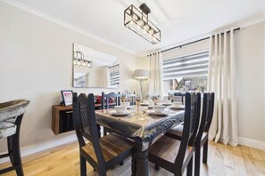 A dining room with a wooden table set for six, six chairs, a chandelier, a mirror, and a window with curtains.
