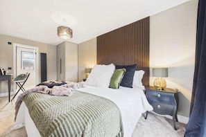 A modern bedroom with a bed, bedside tables, a lamp, and a view through a door.