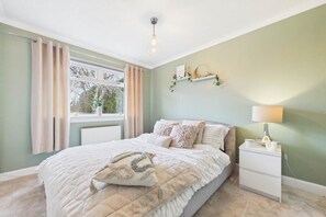 A bedroom with a bed, a nightstand, a window with curtains, a wall-mounted shelf, and a ceiling light.