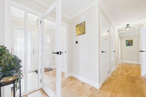 A hallway with white doors, a potted plant, and a painting on the wall.