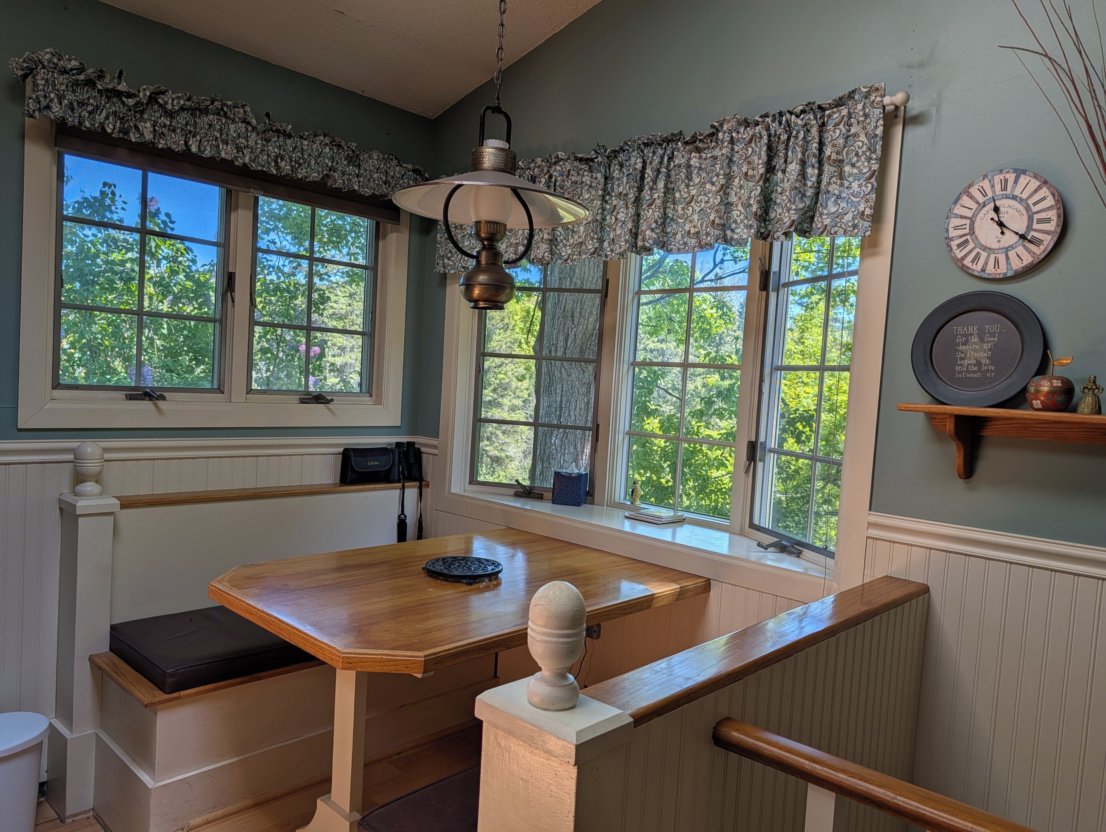 Un coin repas avec une table en bois, des bancs, un luminaire suspendu et une horloge au mur.