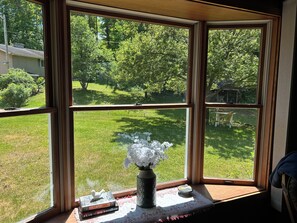 A room with a large window offering a view of a green lawn and trees.