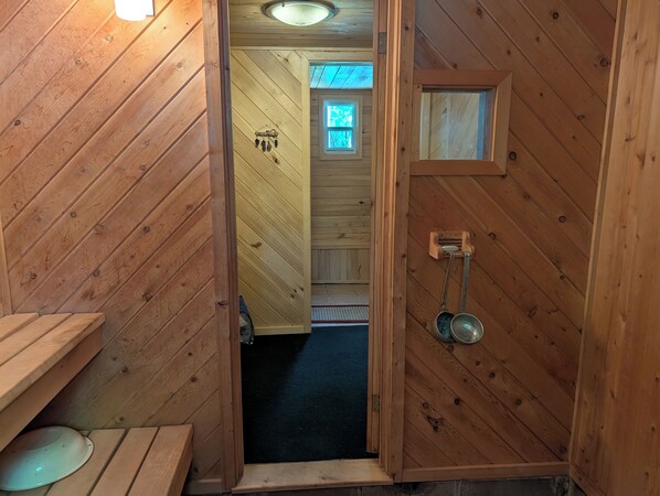 A wooden cabin interior with a door leading to a room, a small window, and a ceiling light.