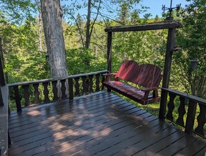 A wooden deck with a bench, surrounded by trees and a weather vane.