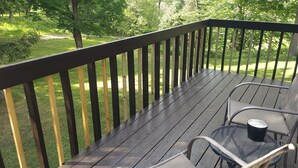 A wooden deck with metal chairs and a table, surrounded by trees and a grassy area.