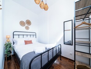Un dormitorio ordenado con cama, lámpara de noche, cestas en la pared y un espejo.