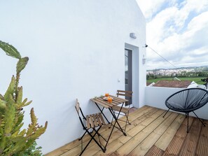 Un balcón con mesa y sillas, una planta de cactus y vistas a un pueblo.