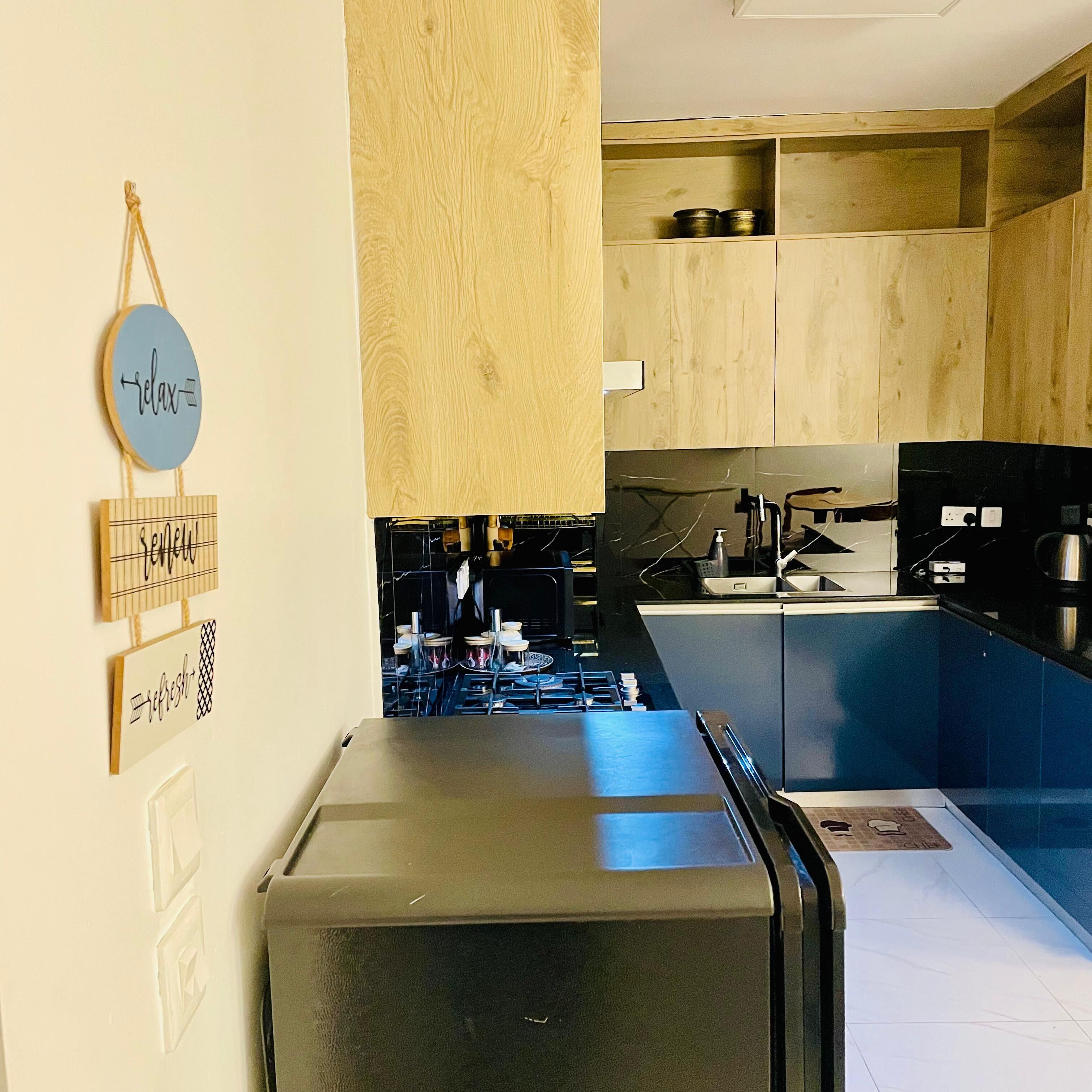 A kitchen with wooden cabinets, a stainless steel refrigerator, and a blue wall-mounted sign with words.