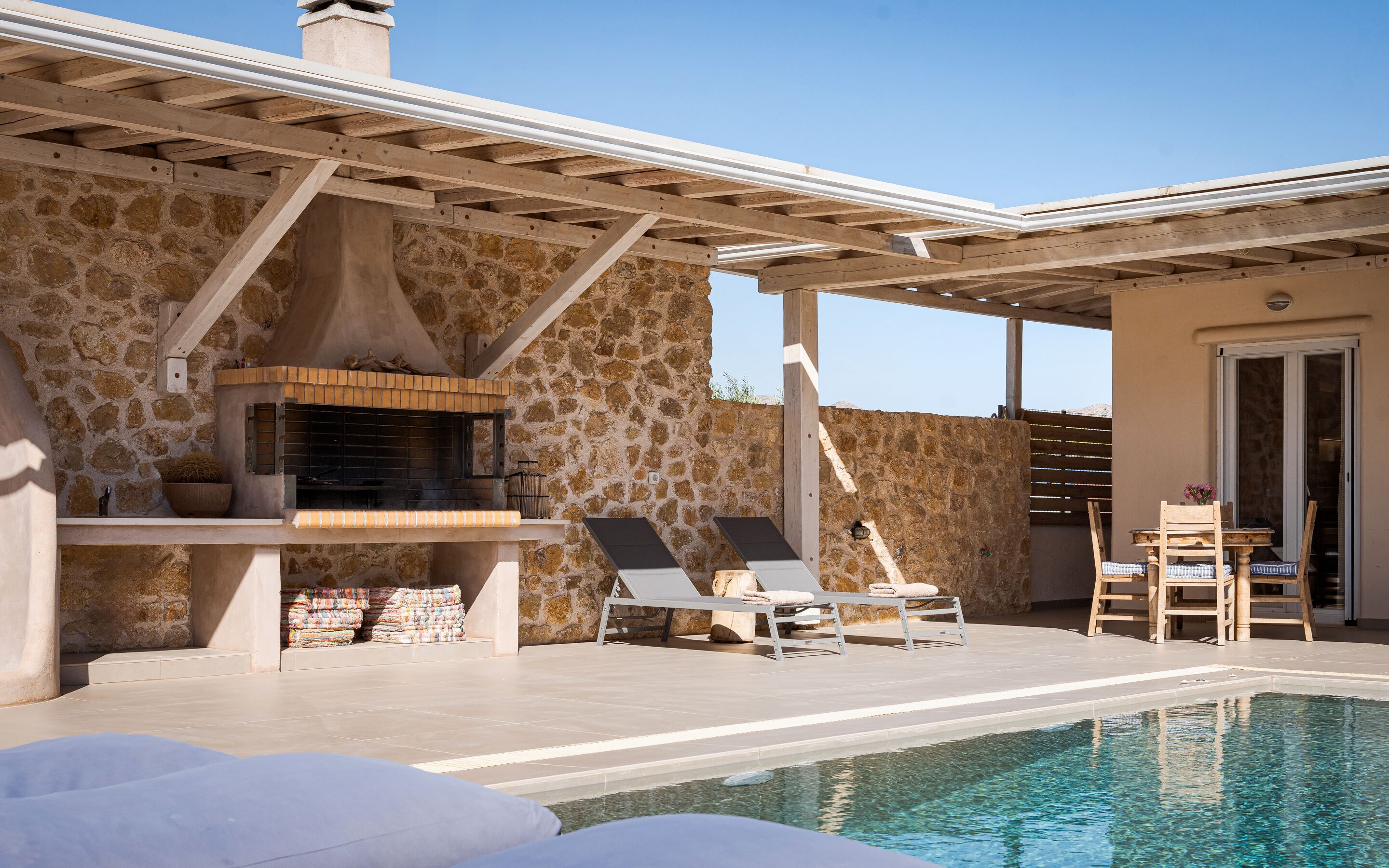 A stone-clad building with a pool, outdoor seating, and a barbecue area.
