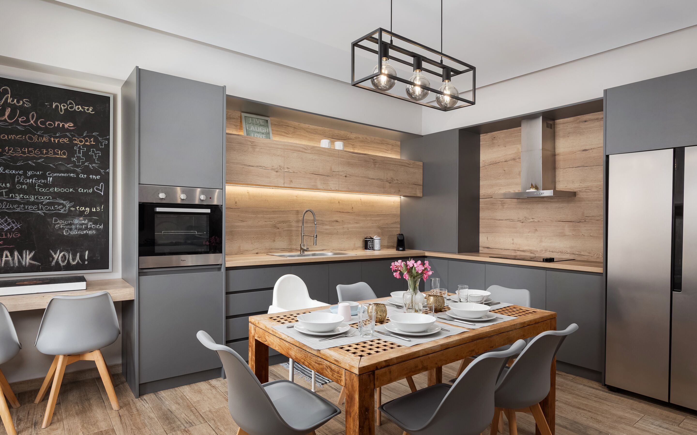 A modern kitchen with a built-in oven, a wooden island with seating, and a chalkboard with writing.