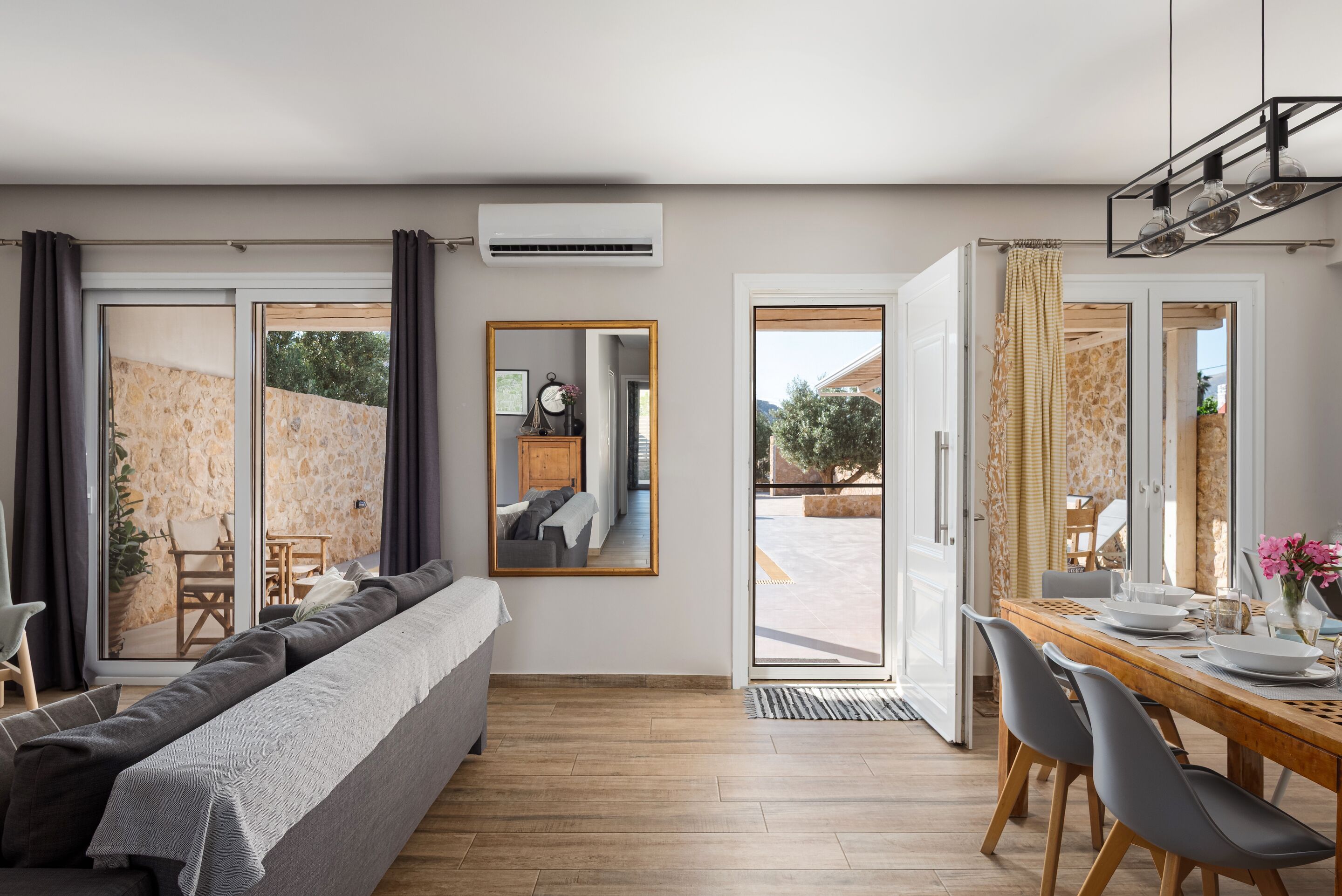 Un salon moderne comprenant un canapé, une table à manger et des chaises, un grand miroir et une porte ouverte donnant sur un balcon.