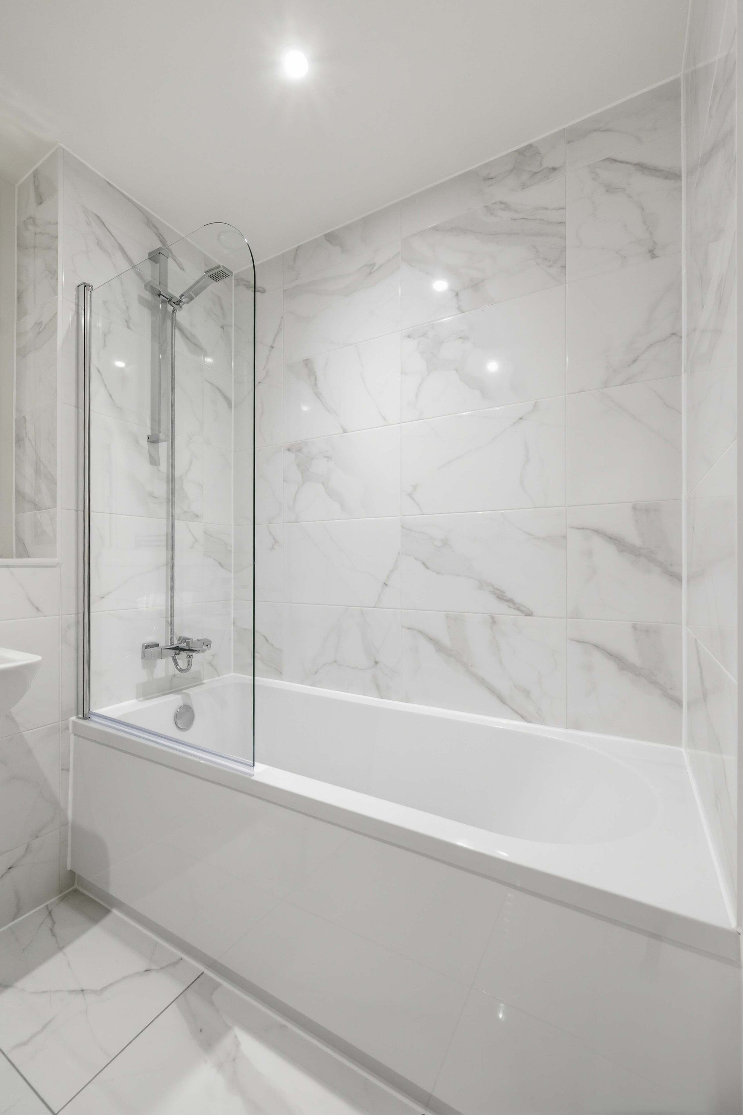 Une salle de bain moderne avec une douche à parois de verre, une baignoire blanche et des murs à motifs de marbre.