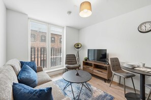 Ein modernes Wohnzimmer mit einer Couch, Sesseln, einem runden Tisch, einem Fernseher und einer Wanduhr.