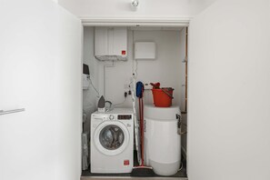 Ein kleiner Hauswirtschaftsraum mit Waschmaschine, Trockner, Warmwasserbereiter und einem Mop.