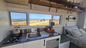 Une cuisine de taille réduite, équipée d’une cuisinière à gaz, d’un évier et d’une fenêtre donnant sur un champ.