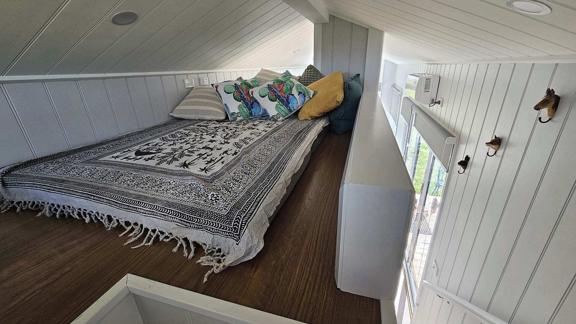 A room with a bed, a patterned rug, and a wall-mounted shelf with hooks.