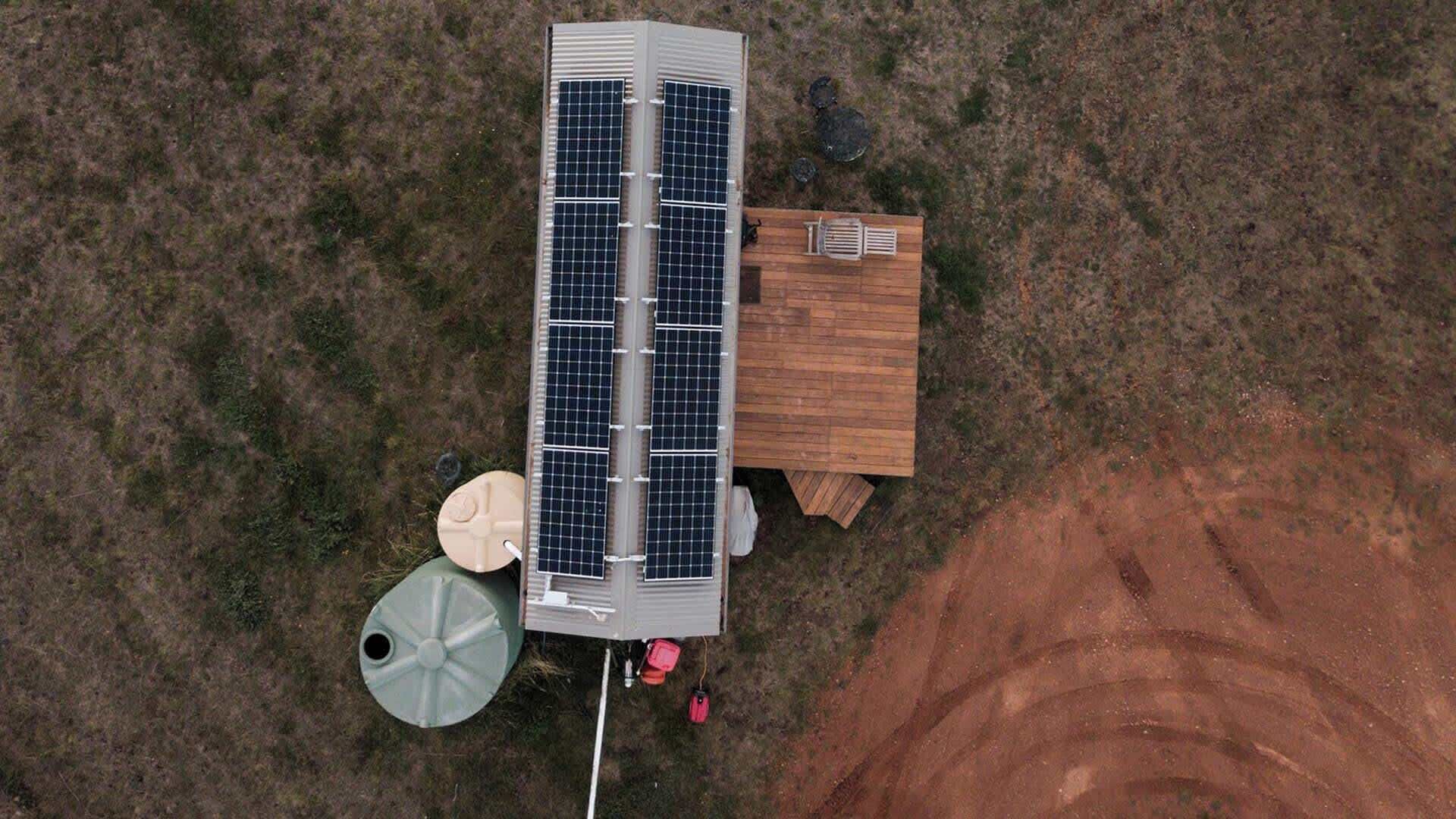 A solar panel installation with a wooden structure, a water tank, and a dirt area.