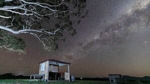 A rustic cabin with a sloped roof, a small porch, and a clear view of the starry night sky.