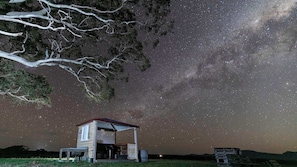 Una cabaña rústica con techo inclinado, un pequeño porche y una vista despejada del cielo estrellado.