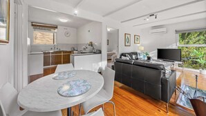 Un ambiente moderno con cucina, zona pranzo e soggiorno, caratterizzato da un divano nero e TV.