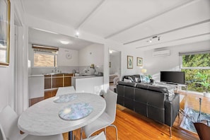 Un espacio habitable moderno con cocina, comedor y sala de estar con sofá negro y televisor.