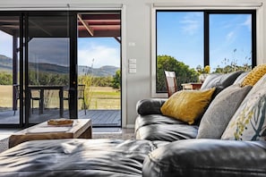 A living room with a sofa, a coffee table, and a view of a deck and mountains.