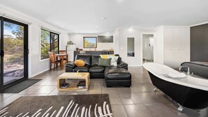A modern living room with a black leather sofa, a wooden coffee table, a black bathtub, and a dining area with a view.