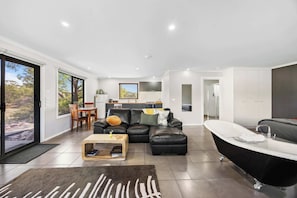 A modern living room with a black leather sofa, a wooden coffee table, a black bathtub, and a dining area with a view.