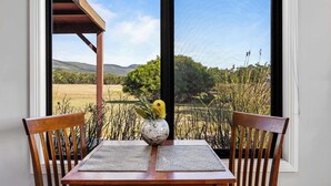 A table with two wooden chairs, a vase with a plant, and a view of a landscape through a window.