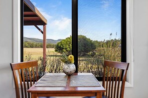 A table with two wooden chairs, a vase with a plant, and a view of a landscape through a window.