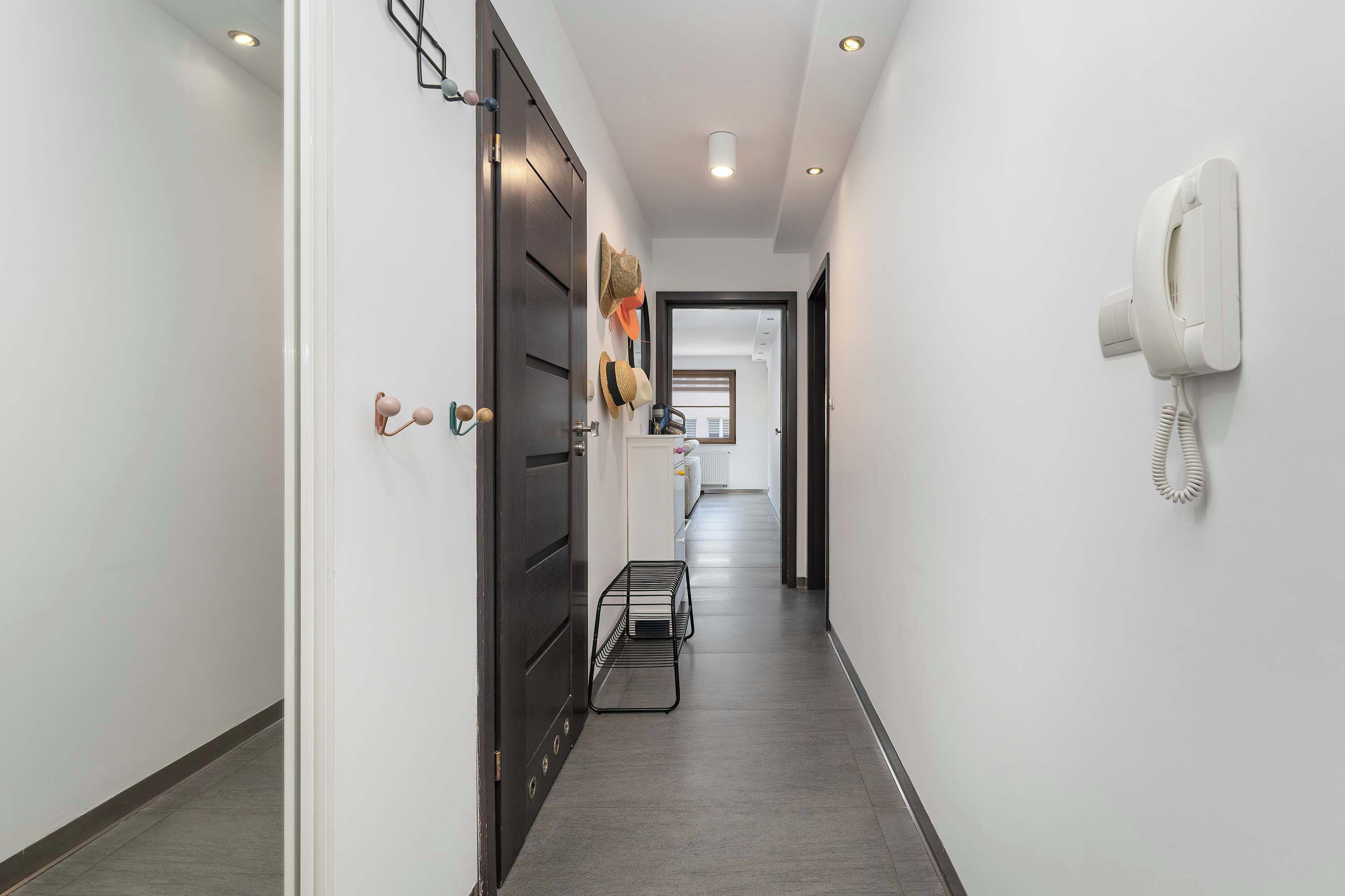 Un couloir avec un téléphone fixé au mur, une porte et un présentoir métallique.
